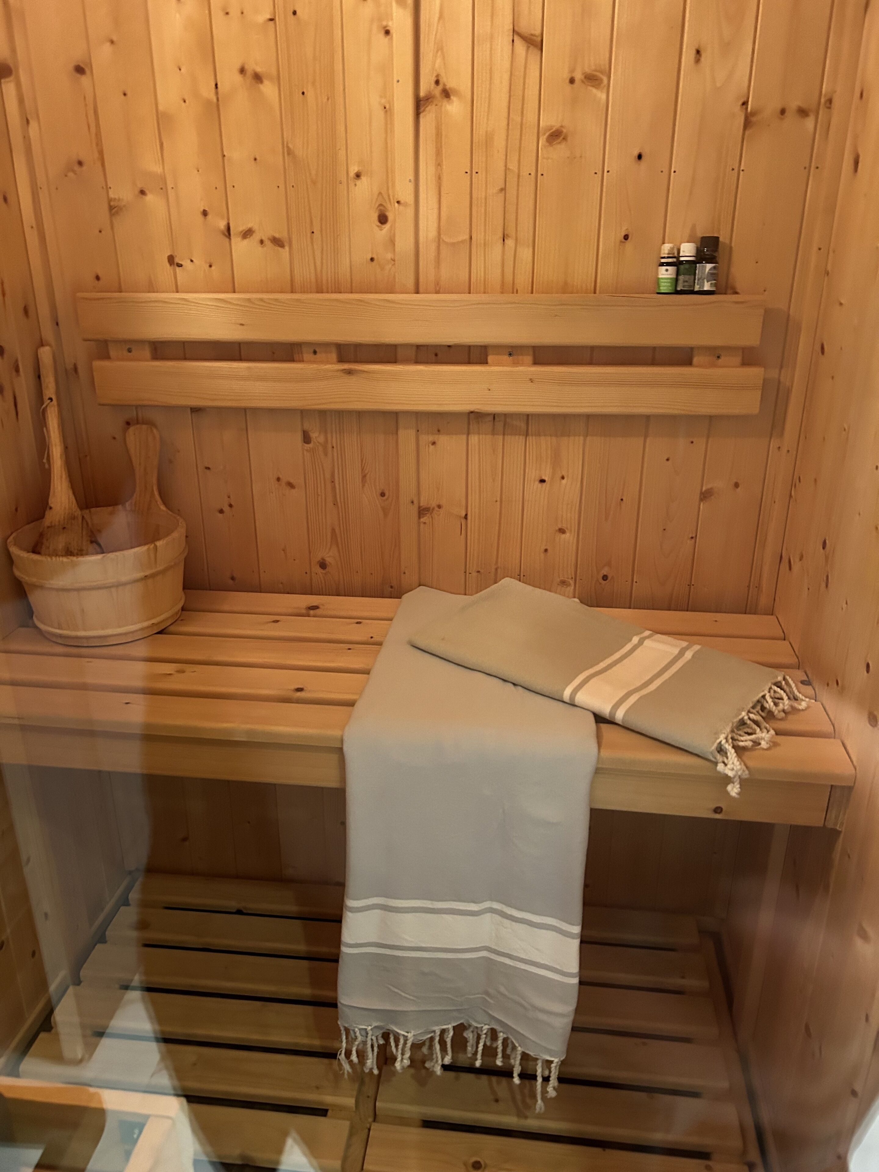 A wooden sauna with benches, a wooden bucket, and a shelf with bottles.