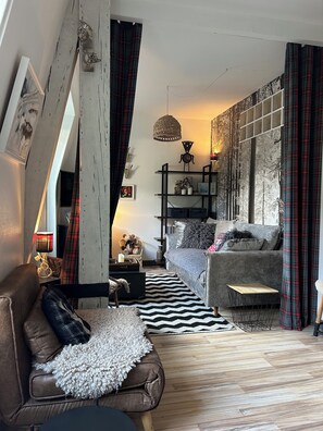 Una sala de estar acogedora con un sofá de cuero marrón, un sofá gris, un alfombra blanco y negro y una mesa de centro de madera. Hay un aparador negro con objetos decorativos y una lámpara colgante de fibras naturales.