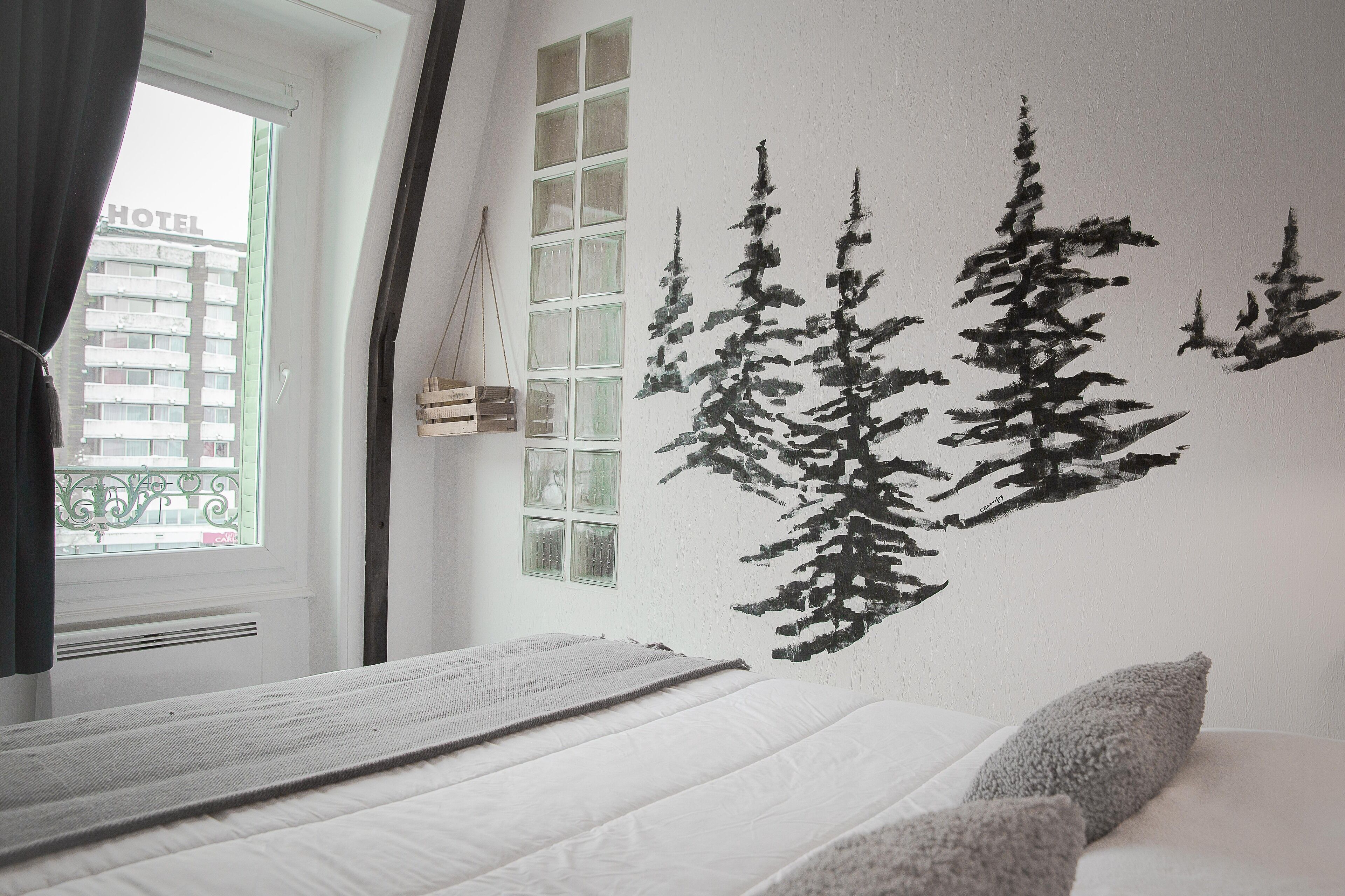 Habitación de hotel con cama, ventana con cortinas y un mural en la pared que representa un bosque.