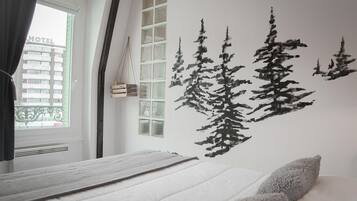 Habitación de hotel con cama, ventana con cortinas y un mural en la pared que representa un bosque.