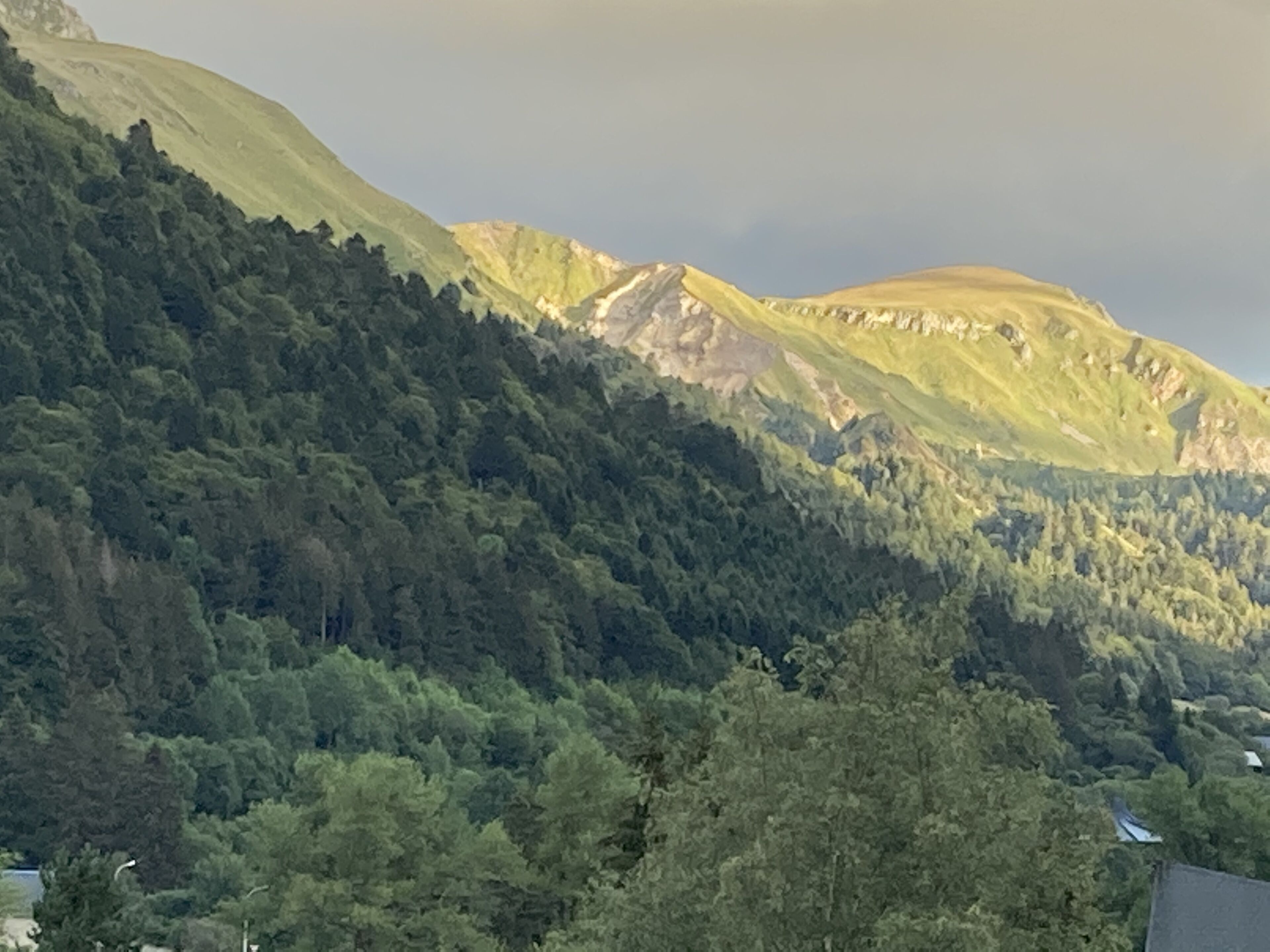 Een bergachtig landschap met dicht bos en enkele zichtbare gebouwen.