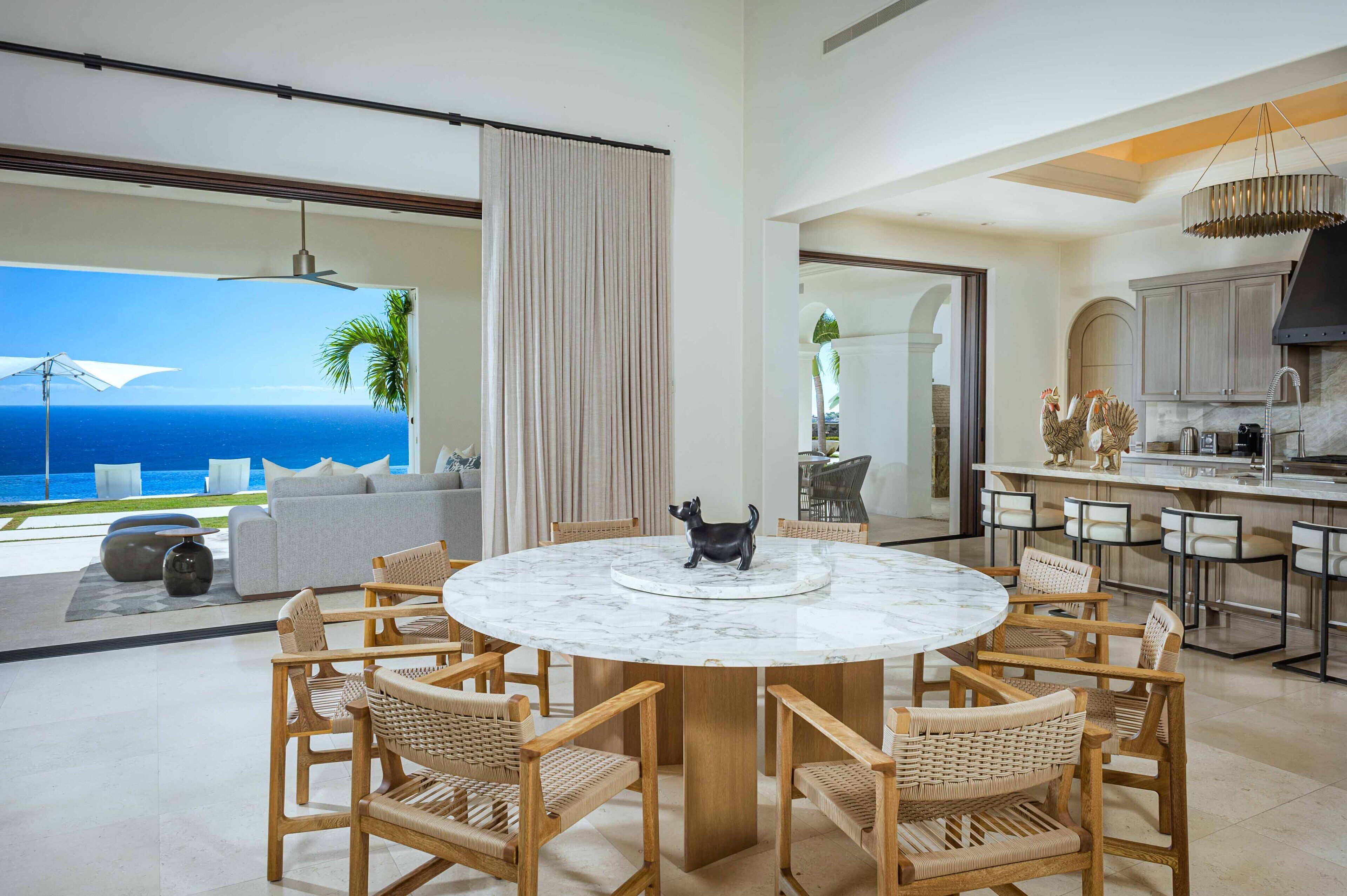 Une cuisine moderne dotée d’un îlot central, d’un coin repas avec une table ronde et des chaises, et offrant une vue sur l’océan.