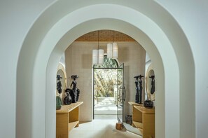A modern bathroom with a central archway, wooden vanity, and a view of a stone wall and greenery outside.