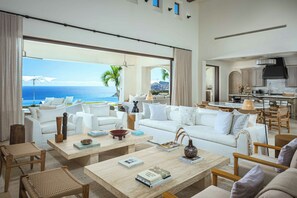 A spacious living area with a large window overlooking the ocean, a kitchen with modern appliances, and a dining area with wooden furniture.