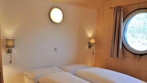 A room with two beds, a round window, and two wall-mounted lights.