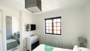Un dormitorio con cama, cómoda, televisor, ventana y baño.