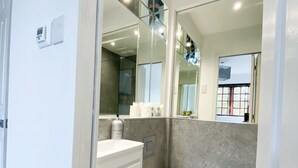 Un baño moderno con inodoro blanco, tocador con espejo y zona de ducha.