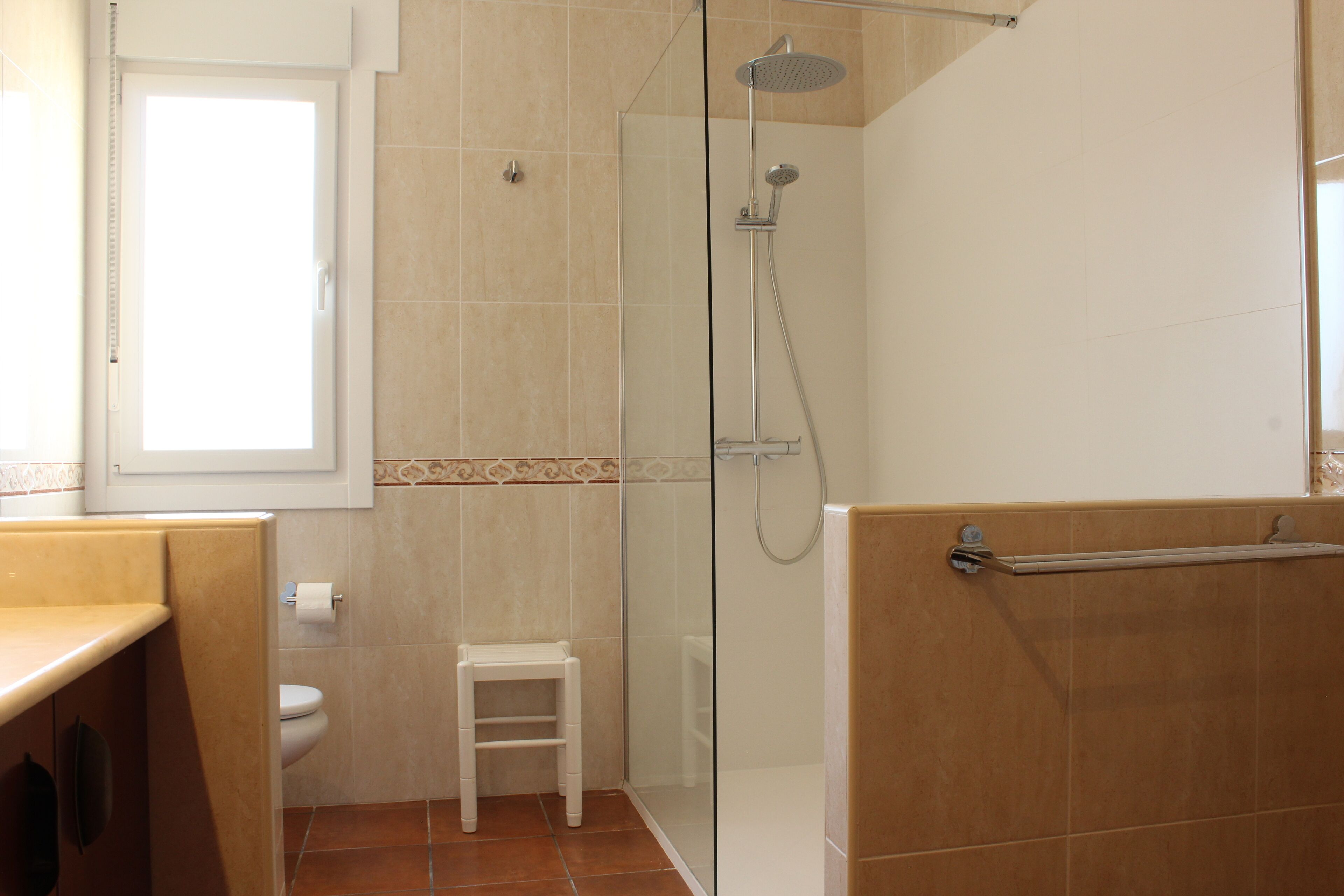 A bathroom with a glass-enclosed shower, a toilet, and a small white stool.