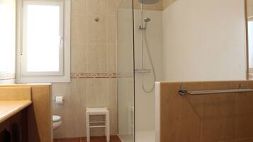 A bathroom with a glass-enclosed shower, a toilet, and a small white stool.