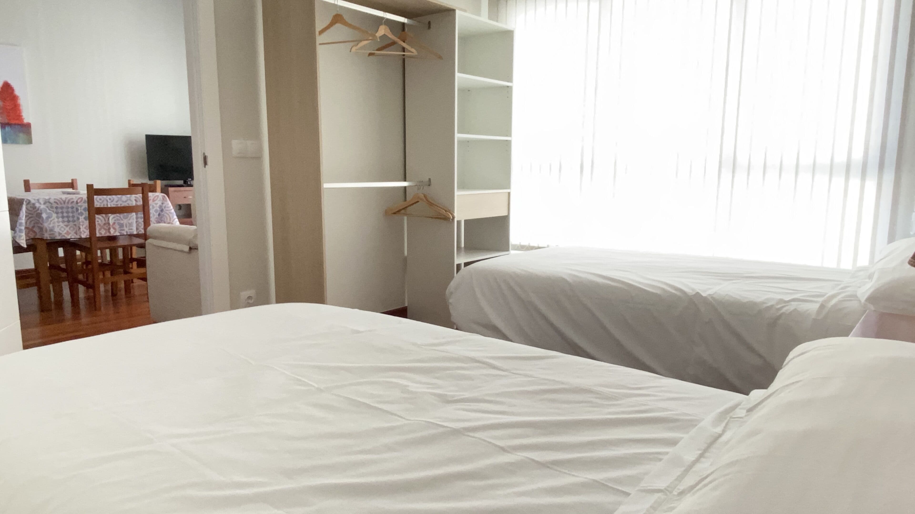 A hotel room with two beds, a dining area with a table and chairs, and a wardrobe with hangers.