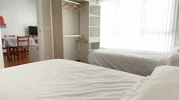 A hotel room with two beds, a dining area with a table and chairs, and a wardrobe with hangers.