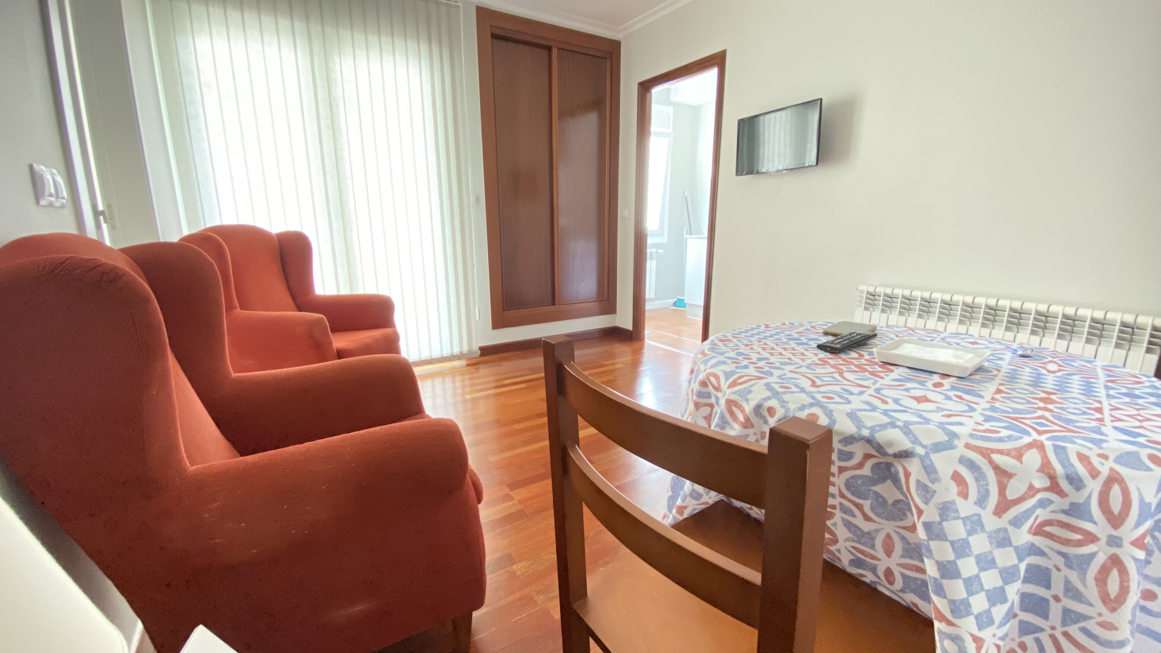 A room with a bed, a TV, and three orange chairs.