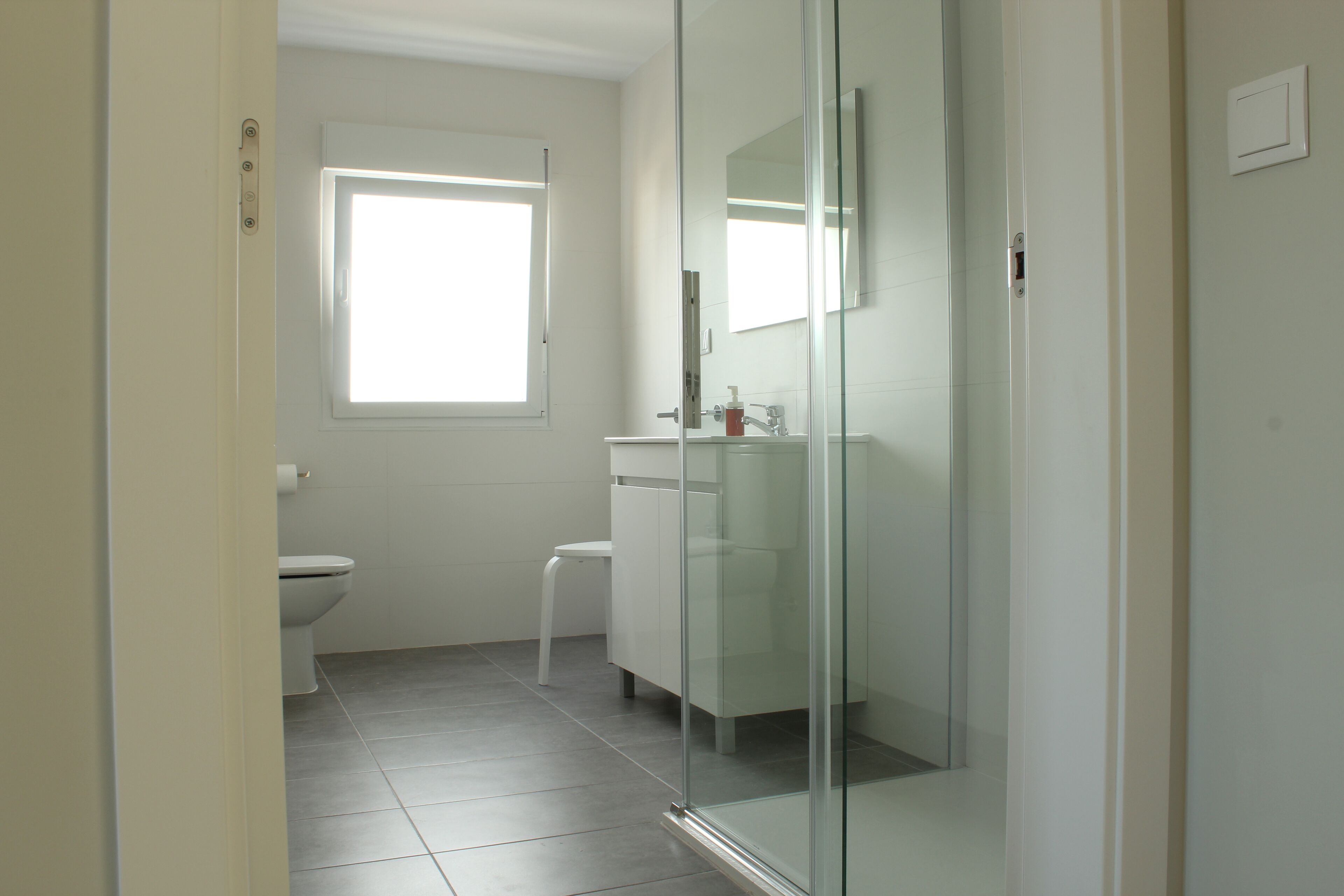 Un baño moderno con inodoro, cabina de ducha de vidrio y ventana que proporciona luz natural.
