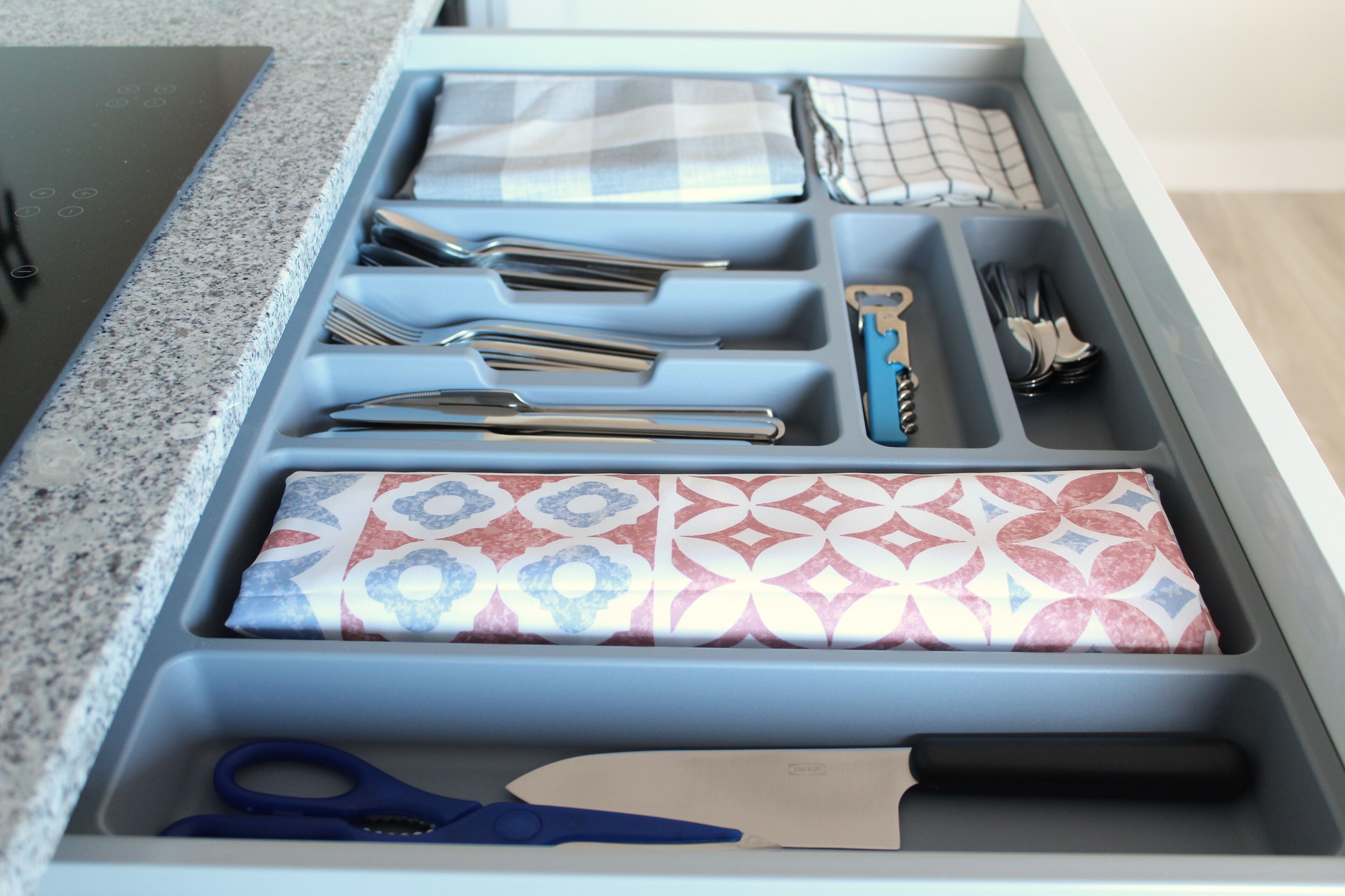 A kitchen drawer with utensils, a knife, and a pair of scissors.