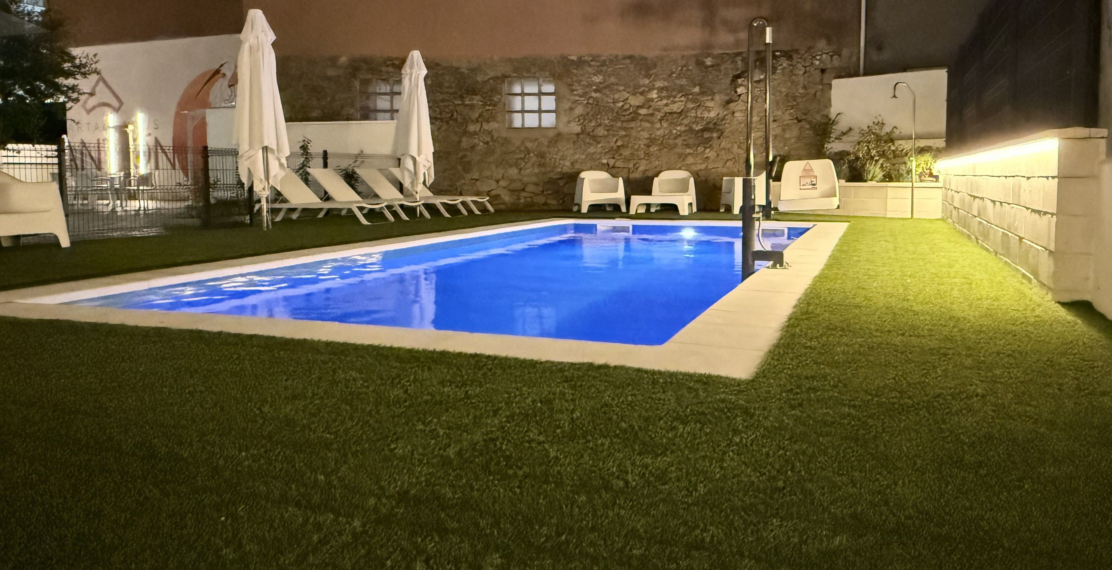 Piscina cercada por grama sintética, cadeiras de descanso e guarda-sóis.