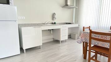 A modern kitchen with white cabinetry, a built-in microwave, and a sink. There's a small table with a patterned tablecloth and a chair.