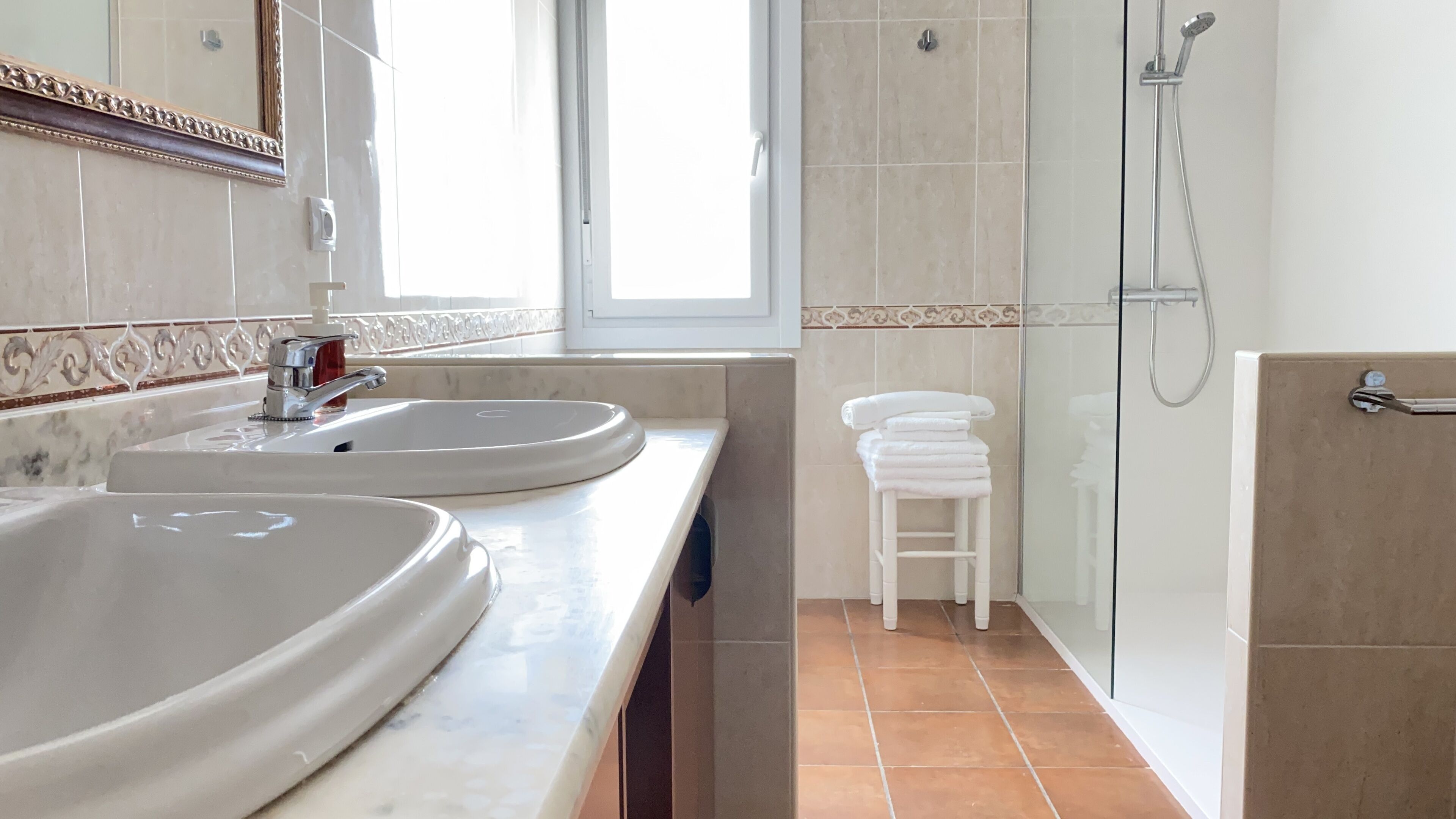 A bathroom with two sinks, a shower, and a window.