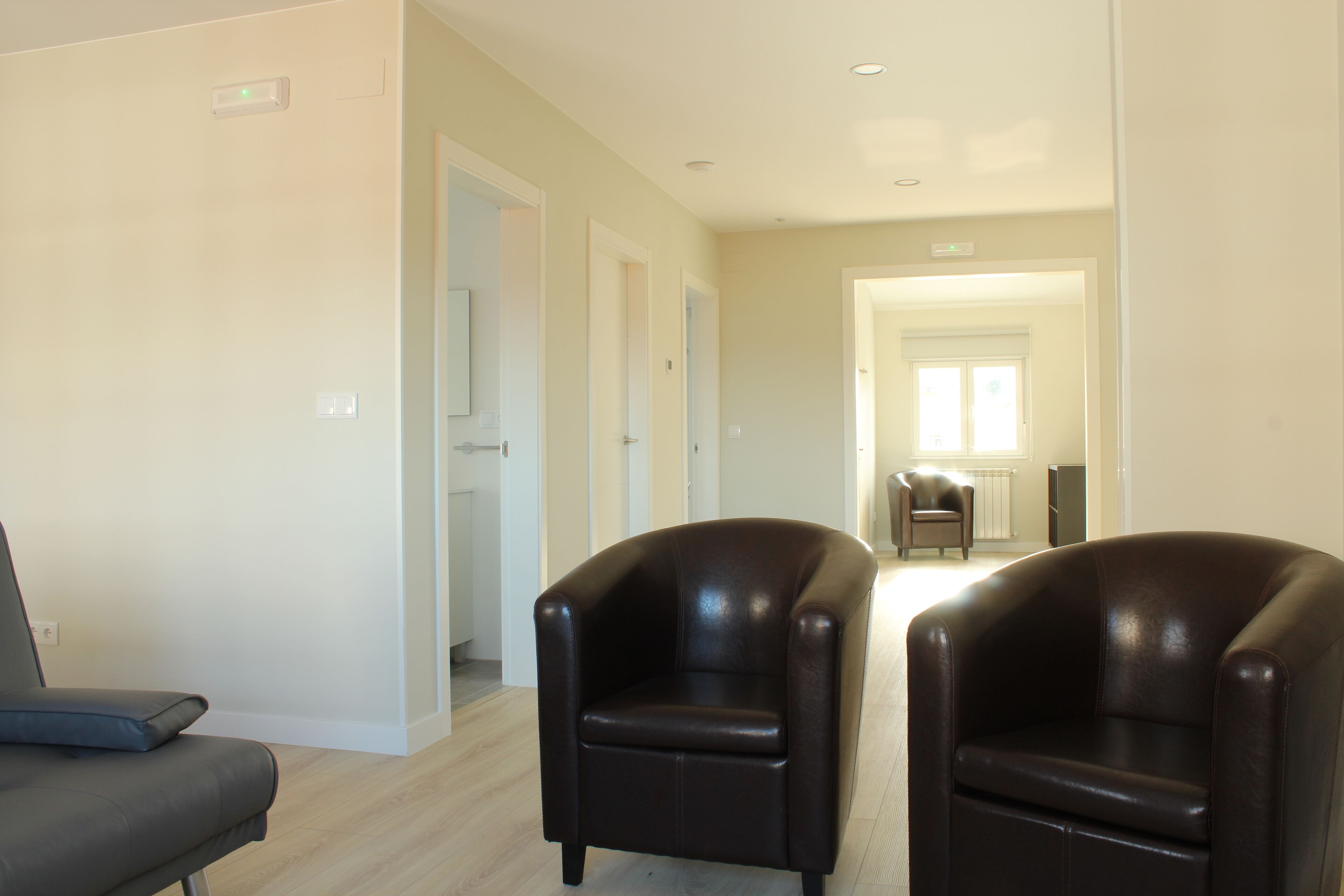 A spacious room with two black leather chairs, a grey sofa, and a wooden floor.