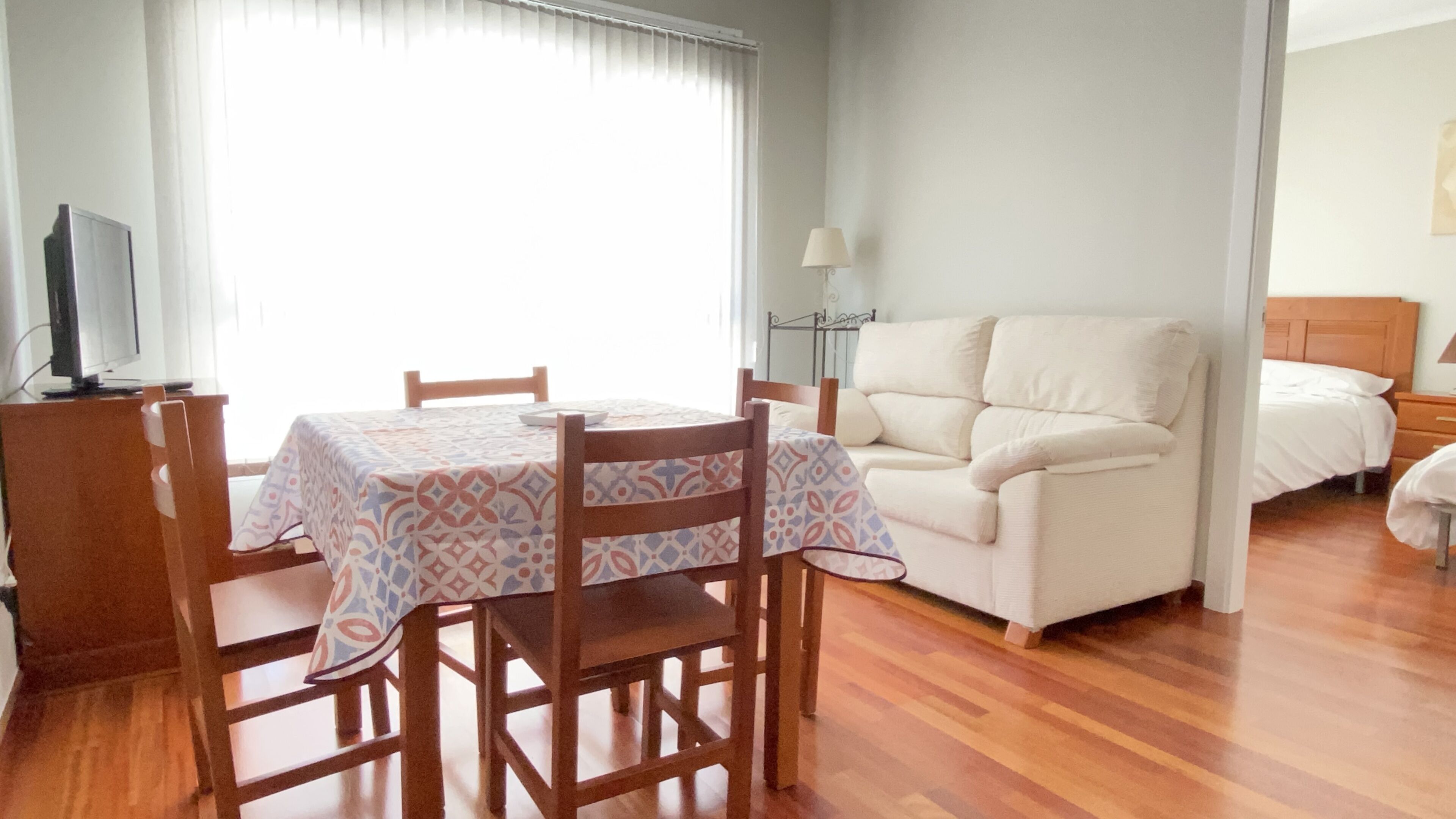 Una habitación con una mesa de comedor, sillas, un sofá, un televisor y una lámpara.