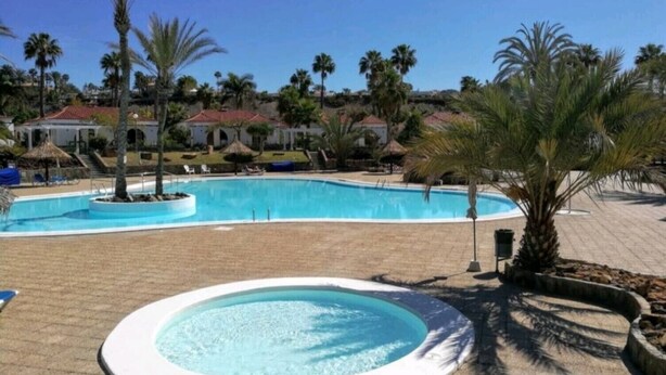 A swimming pool with a surrounding deck, palm trees, and buildings in the background. - Excellent bungalow in Maspalomas (Maspalomas)