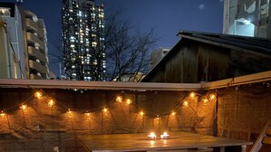 An outdoor seating area with a wooden table and chairs, string lights, and a brick wall. - 2-minute walk from Tenjinbashisuji Rokuchome Station! A house with a rooftop terrace 2 min. from Tenma Izakaya district 10 min. from Umeda 15 min. from Namba Max. 13 persons (大阪市北区)