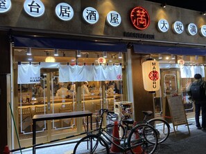 A restaurant with a neon sign, bicycles parked outside, and a signboard with contact information.