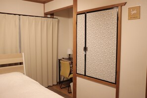 A hotel room with a bed, a chair, a desk with a lamp, and a sliding door with a 'No Smoking' sign.