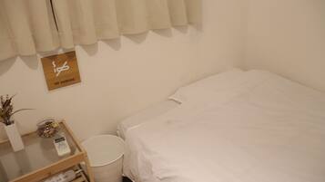 A small, clean room with a bed, a bedside table with a lamp, a trash bin, and a 'No Smoking' sign on the wall.