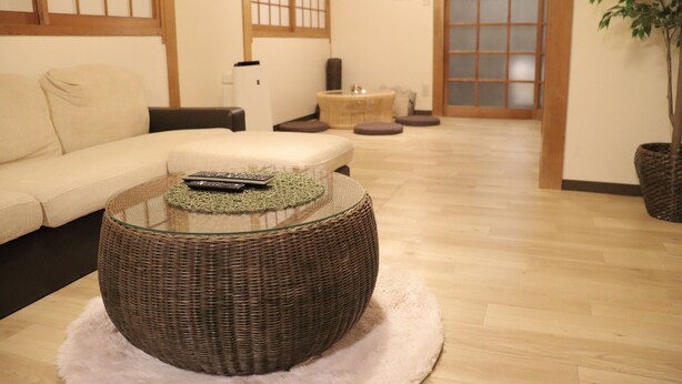A modern living room with a round wicker coffee table, a beige sofa, and a traditional Japanese sliding door in the background. - 2-minute walk from Tenjinbashisuji Rokuchome Station! A house with a rooftop terrace 2 min. from Tenma Izakaya district 10 min. from Umeda 15 min. from Namba Max. 13 persons (大阪市北区)