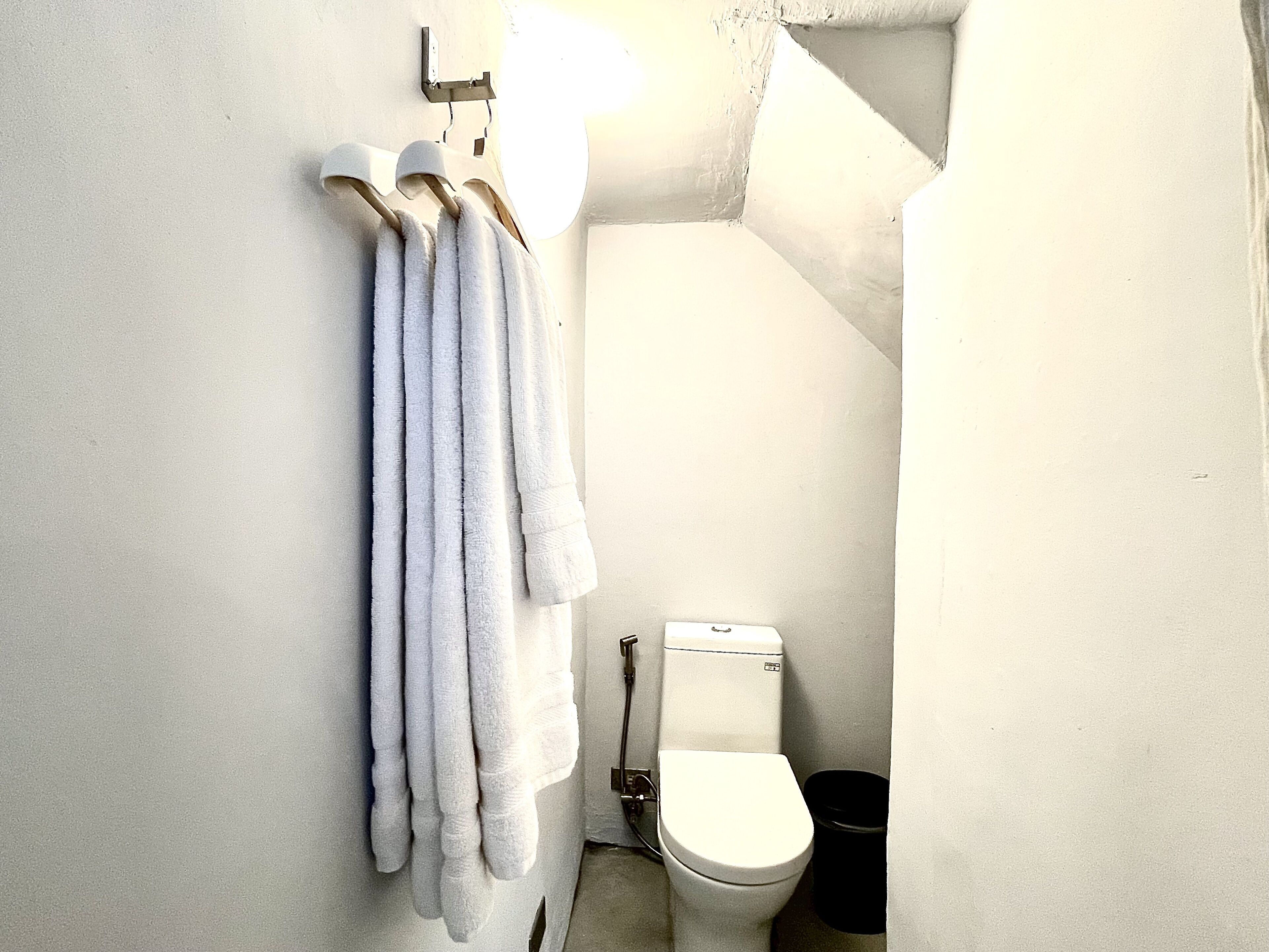 Ein Badezimmer mit Toilette, einem schwarzen Mülleimer und einem Handtuchhalter mit mehreren Handtüchern.