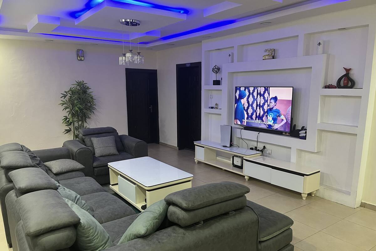 A modern living room with a sectional sofa, a coffee table, and a flat-screen TV mounted on a white wall.