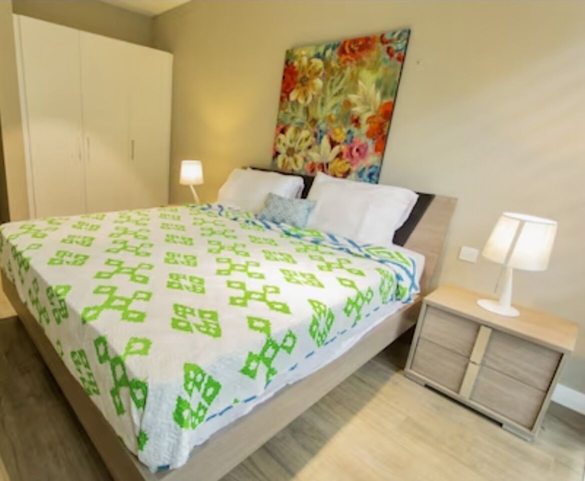 A bedroom with a bed, nightstands, a wardrobe, and a floral painting on the wall.