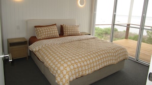 Une chambre avec un grand lit, deux tables de chevet et une vue sur la mer, accessible par une porte-fenêtre coulissante.
