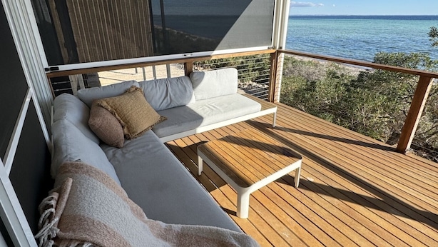 Un balcon avec un canapé, une table en bois et une vue sur l’océan.