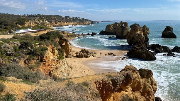 A coastal landscape with rocky formations, a sandy beach, and a clear sky.