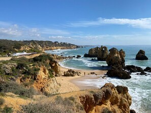 A coastal landscape with rocky formations, a sandy beach, and a clear sky.