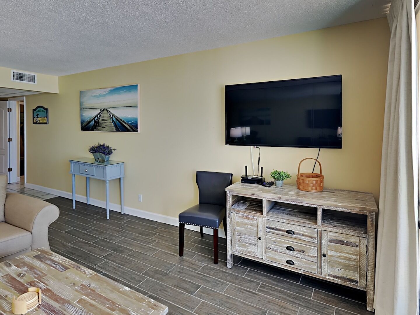 A living room with a TV, a painting, a small table with a plant, a chair, and a wooden entertainment center.