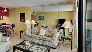 Un salon comprenant un canapé, deux tables d’appoint avec des lampes, une table basse en verre et un coin repas avec des chaises et une table.