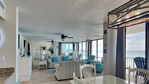 A spacious living area with a view of the ocean, a dining table, and a kitchen area.
