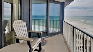 A balcony with a chair, a glass door, and a view of the beach.