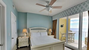 Un dormitorio con cama, mesitas de noche, ventilador de techo y balcón con vista al océano.