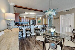 A dining area with a glass table and chairs, wooden flooring, and a decorative ceiling light.