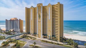 Un hotel moderno de gran altura con múltiples balcones, vista al mar y un área de estacionamiento.