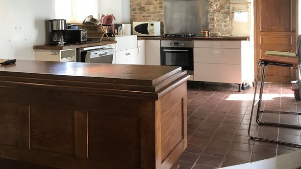 A kitchen with a large wooden island, a stone wall, and a hanging light fixture.