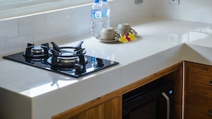 A kitchen with white tiles, a gas stove, a window, and a light fixture. - Donguri House Bali (Kedonganan)