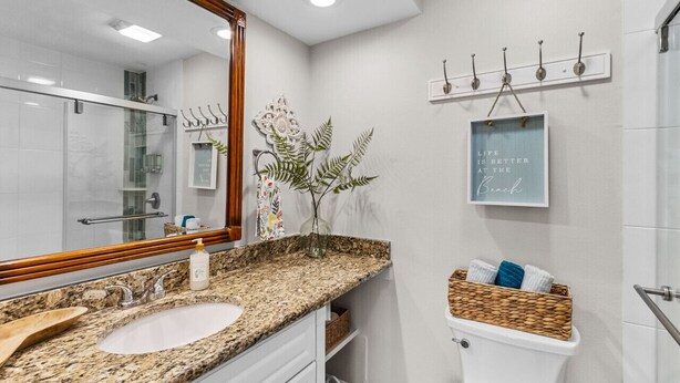 A modern bathroom with a granite countertop sink, a large mirror, a decorative plant, a framed inspirational quote, and a towel rack.