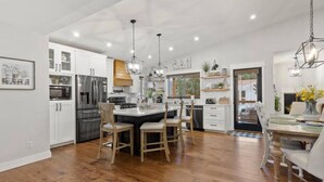 A modern kitchen with white cabinets, stainless steel appliances, and a central island with chairs. - 123 Washington · Charming Modern Farmhouse Style Home in Downtown Monument (Monument)