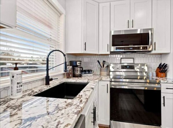 A modern kitchen with white cabinets, a stainless steel microwave, an oven, and a marble countertop.