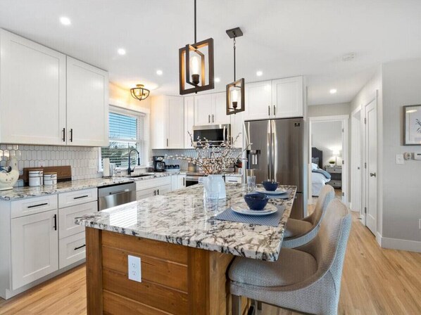 A modern kitchen with white cabinets, a marble island, stainless steel appliances, and pendant lighting.