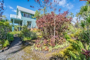 Stroll through the serene garden, featuring a meandering stream and lush greenery, to the charming house with a balcony.